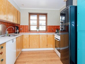 Uma cozinha com armários de madeira, pia de aço inoxidável, janela com vista e refrigerador azul-turquesa.