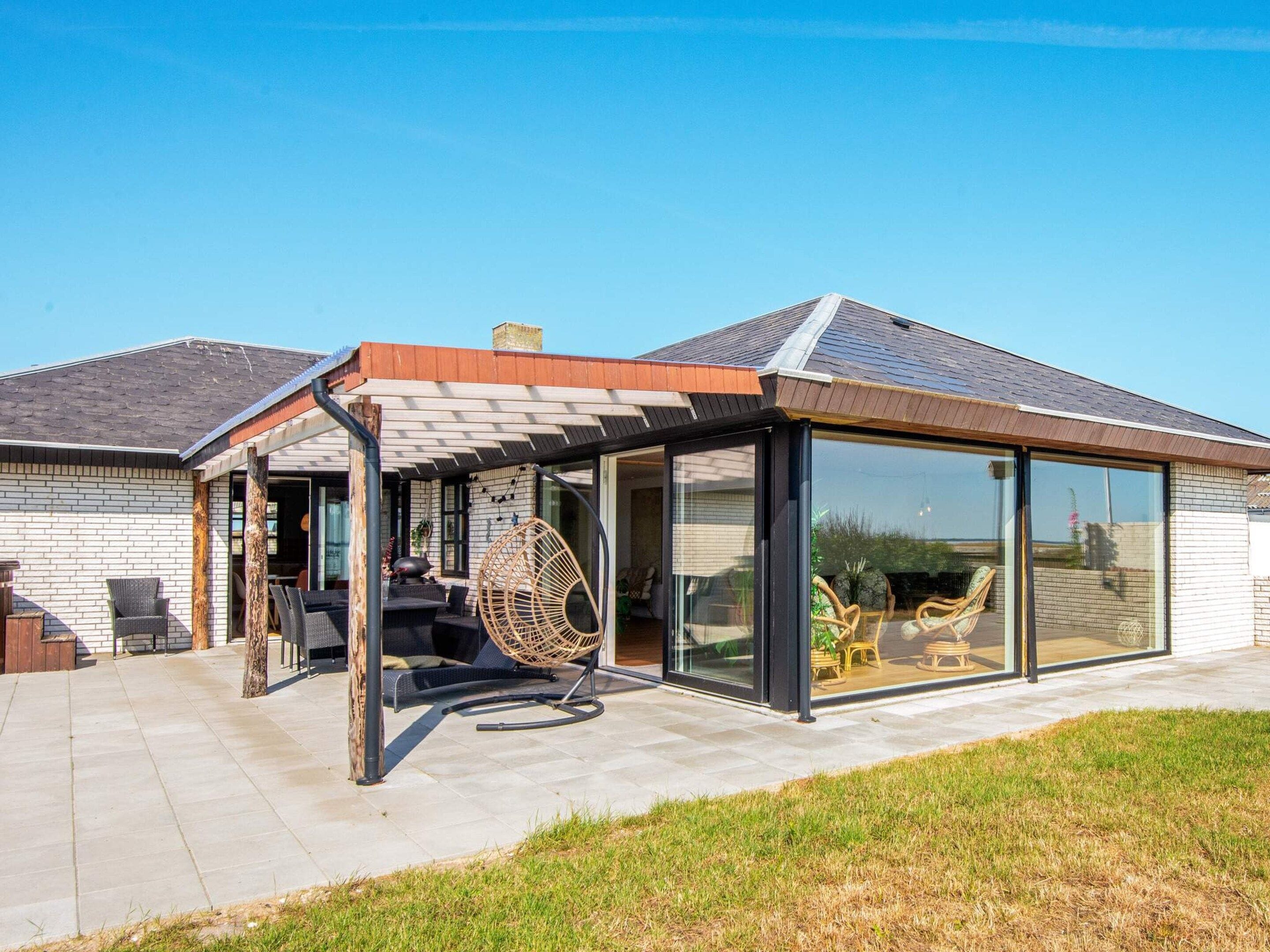 A modern house with a covered patio area featuring outdoor furniture and a swing chair.