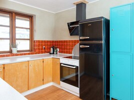 A kitchen with wooden cabinets, a black refrigerator, a stove, and a window with a plant.