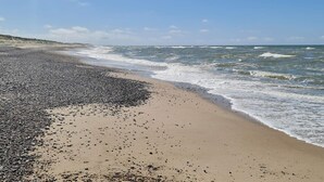Uma praia com pedras e areia, ondas e céu claro.