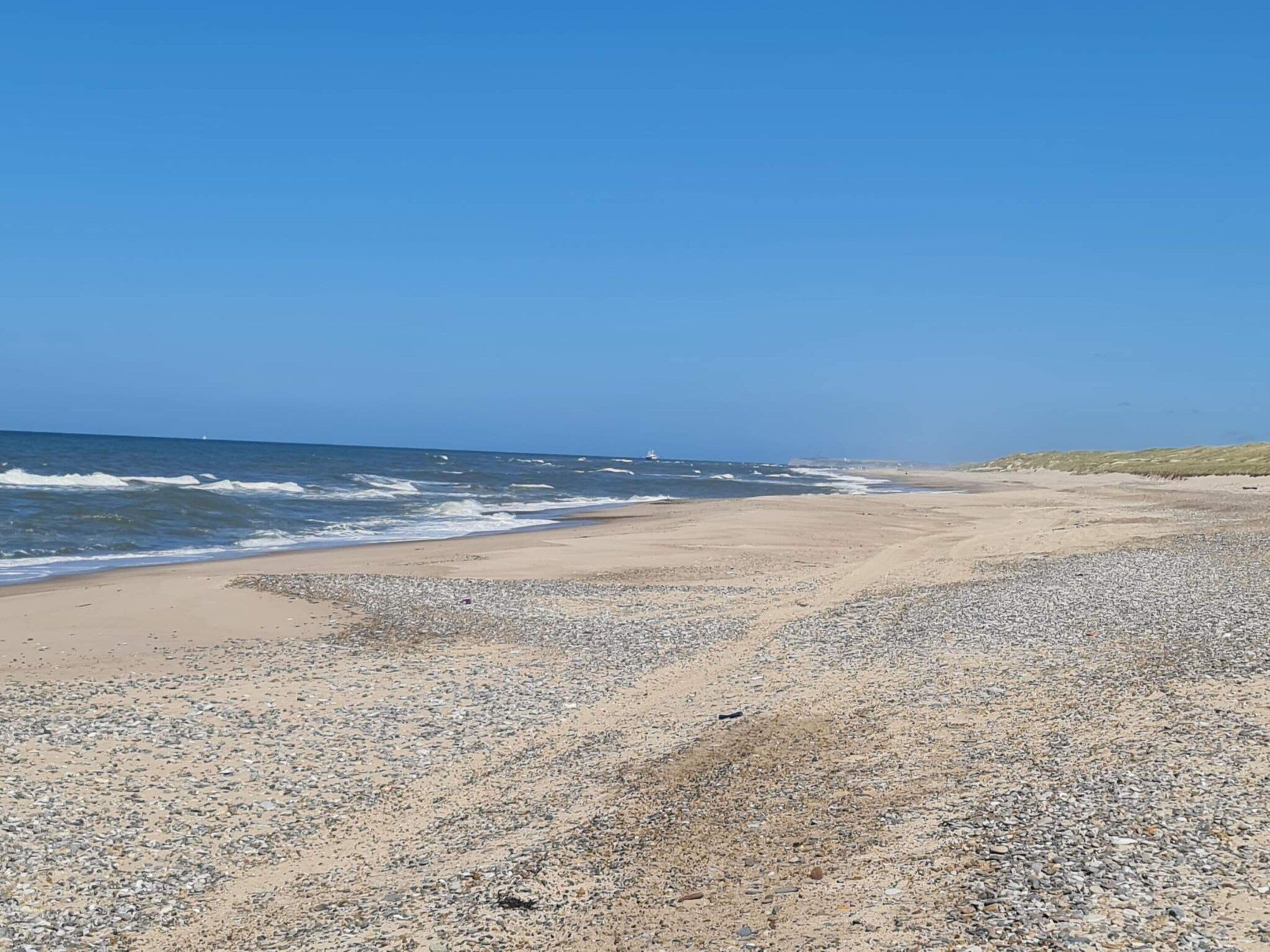 Une plage de galets, avec des vagues et un ciel dégagé.
