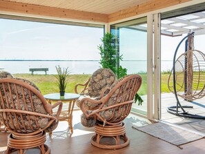 A room with wicker chairs, a glass table, and a view of a lake. - 8 Person Holiday Home in Ulfborg (Ulfborg)