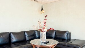 Uma sala de estar moderna com um sofá de couro preto, uma mesa de centro de vidro e um vaso com flores secas.