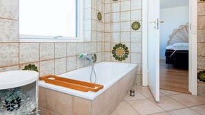 Ein Badezimmer mit einer Badewanne, einem Fenster und einer Tür zu einem Schlafzimmer.