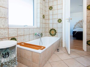 A bathroom with a bathtub, a window, and a door leading to a bedroom. - 8 Person Holiday Home in Ulfborg (Ulfborg)