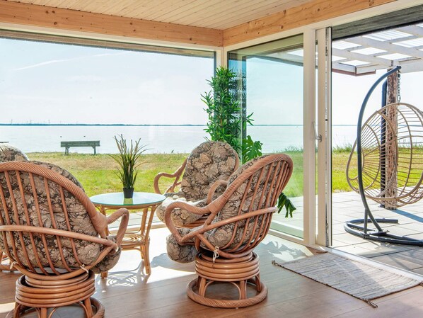 A room with wicker chairs, a small table, and a view of a body of water. - 8 Person Holiday Home in Ulfborg (Ulfborg)