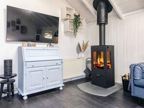 A living room with a black wood-burning stove, a white cabinet, a TV, and a blue sofa. - 6 Person Holiday Home in Vaeggerlose (Vaeggerlose)