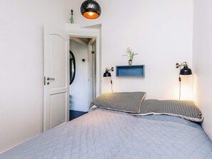 A bedroom with a bed, two bedside lamps, a wall-mounted shelf with a plant, and a door leading to another room. - 6 Person Holiday Home in Vaeggerlose (Vaeggerlose)