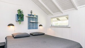 A bedroom with a large bed, two wall-mounted lamps, a window with blinds, and a wall-mounted shelf with a plant and decorative items. - 6 Person Holiday Home in Vaeggerlose (Vaeggerlose)