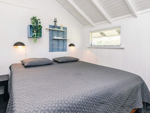 A bedroom with a large bed, two wall-mounted lamps, a window with blinds, and a wall-mounted shelf with a plant and decorative items. - 6 Person Holiday Home in Vaeggerlose (Vaeggerlose)