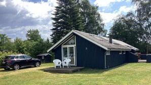 A small, dark-colored cabin with a covered porch and two white chairs. - 6 Person Holiday Home in Vaeggerlose (Vaeggerlose)