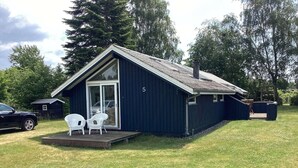 A small, dark-colored cabin with a single door and a small porch area with two white chairs. - 6 Person Holiday Home in Vaeggerlose (Vaeggerlose)