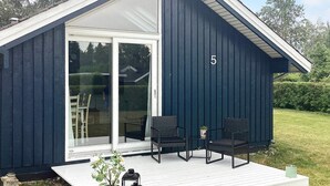 A small, dark blue cabin with a white exterior and a number '5' on the side. It features a glass door leading to a deck with two chairs and a potted plant. - 6 Person Holiday Home in Vaeggerlose (Vaeggerlose)