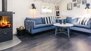 A cozy living room with a fireplace, a blue sofa, a round table, and wall art. - 6 Person Holiday Home in Vaeggerlose (Vaeggerlose)
