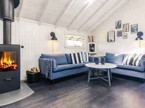 A cozy living room with a fireplace, a blue sofa, a round table, and wall art. - 6 Person Holiday Home in Vaeggerlose (Vaeggerlose)