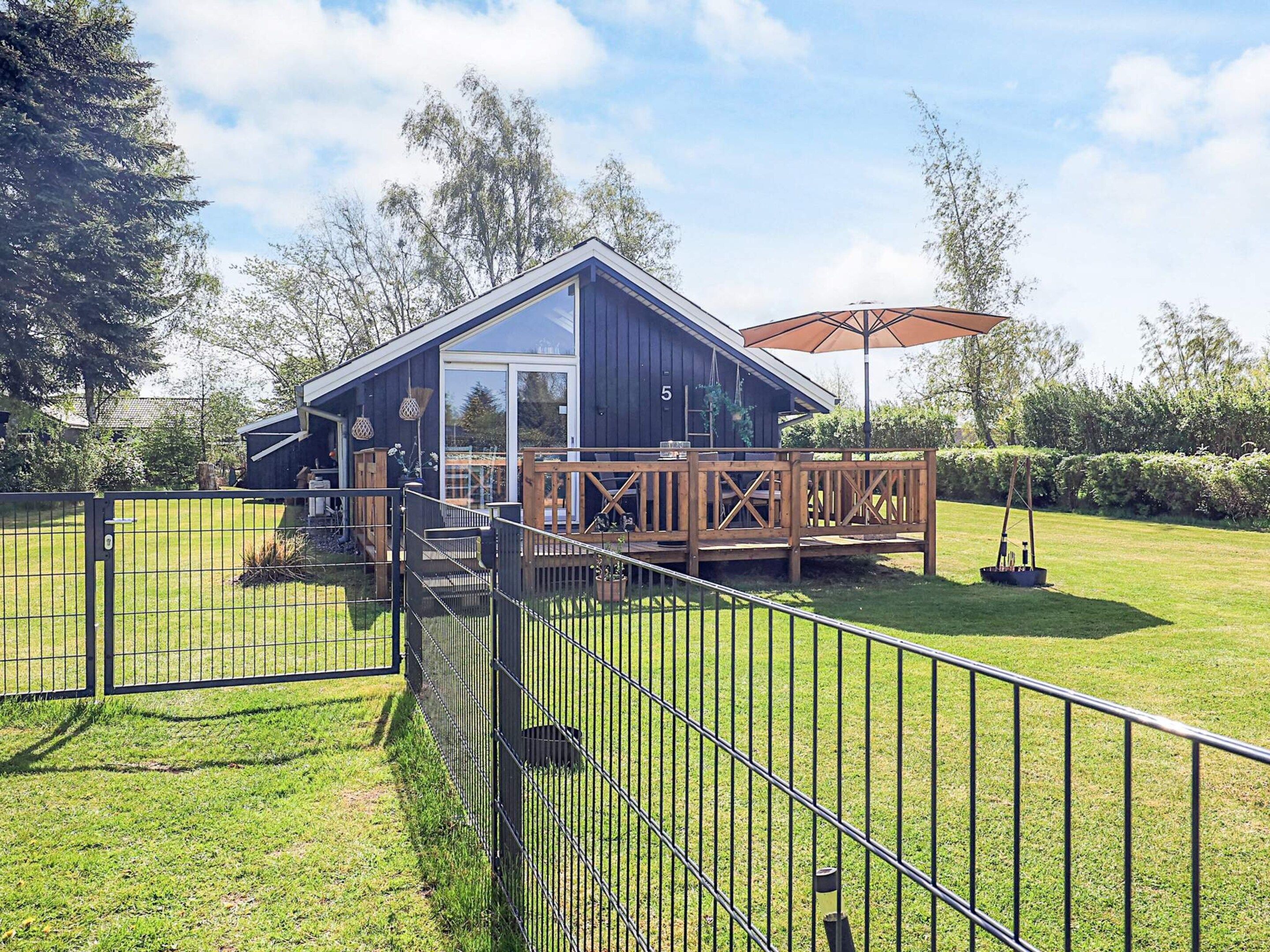 A wooden cabin with a deck, a fenced yard, and a large umbrella.