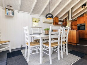 A dining area with a white table and chairs, a black and white rug, and a ceiling with exposed beams. - 6 Person Holiday Home in Vaeggerlose (Vaeggerlose)