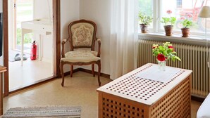 A room with a wooden chair, a table with a vase of flowers, a radiator, and a window with potted plants. - 6 Person Holiday Home in Laholm (Laholm)