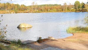 A picnic table by a lake with a sandy shore and trees in the background. - 6 Person Holiday Home in Laholm (Laholm)