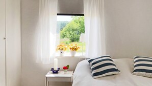 A bedroom with a bed, a small bedside table with a vase of flowers, and a window with curtains. - 6 Person Holiday Home in Laholm (Laholm)