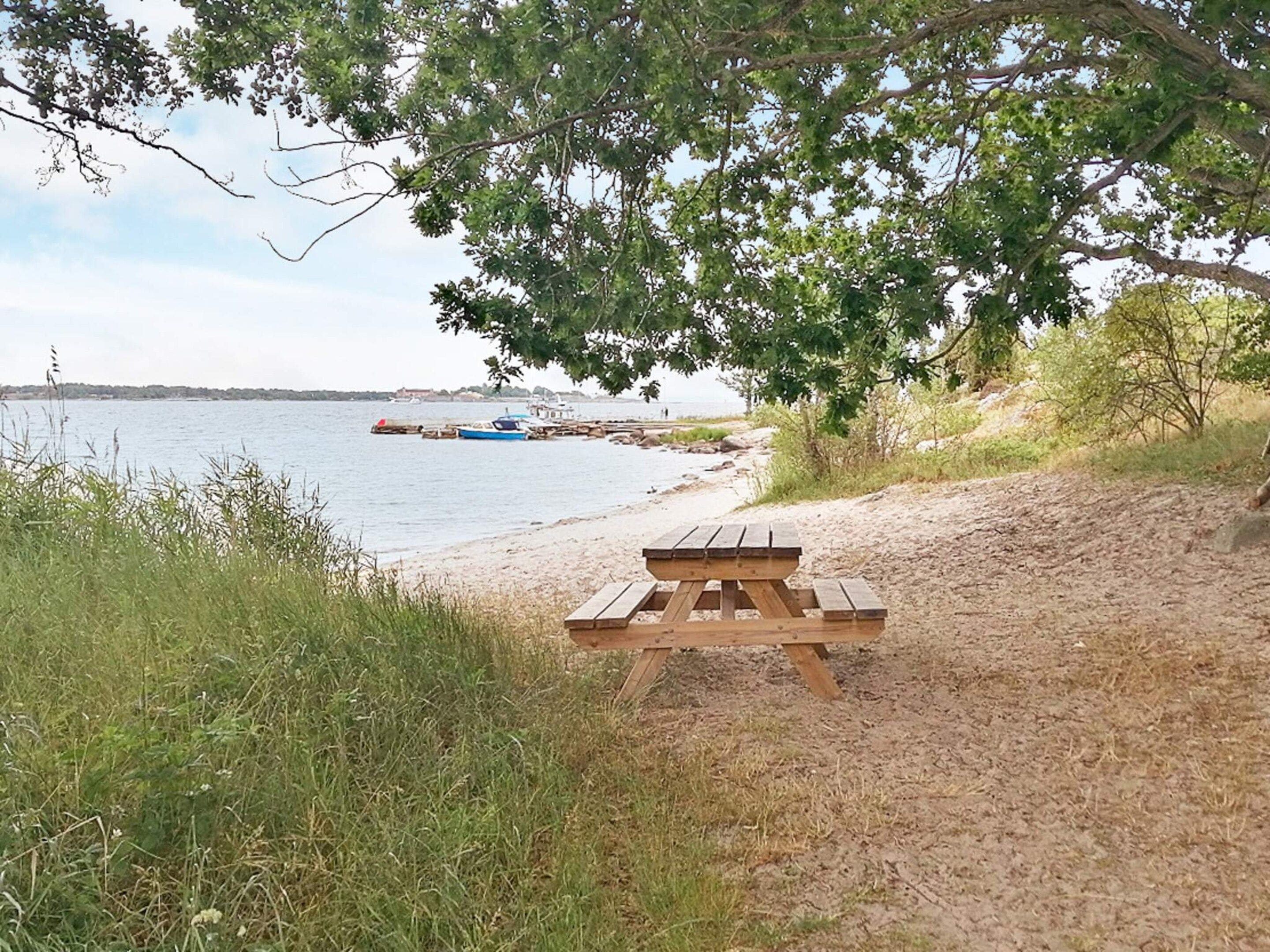 A beach with a picnic table and boats in the background.