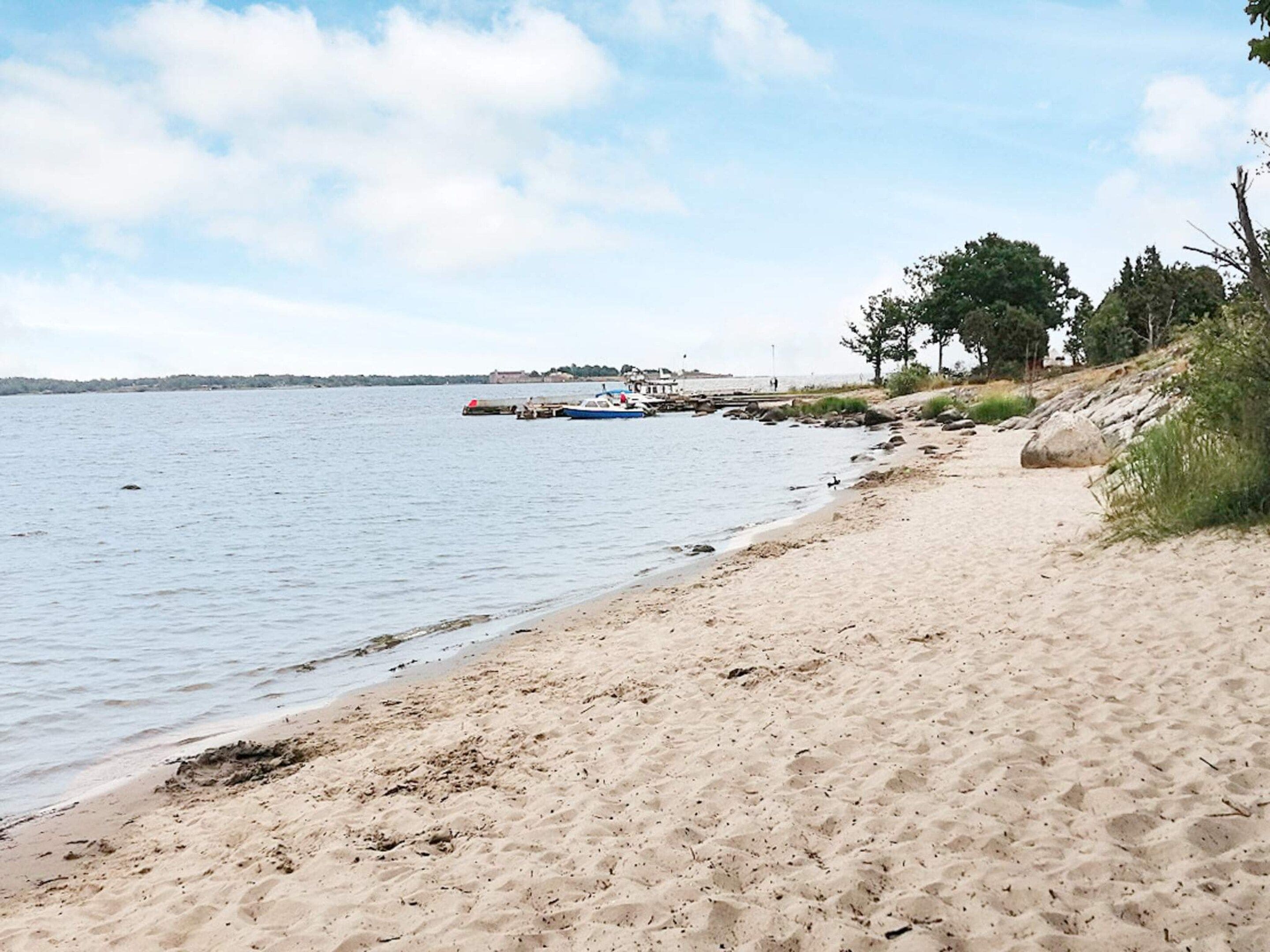 A sandy beach with a calm sea, a pier with boats, and trees in the background.
