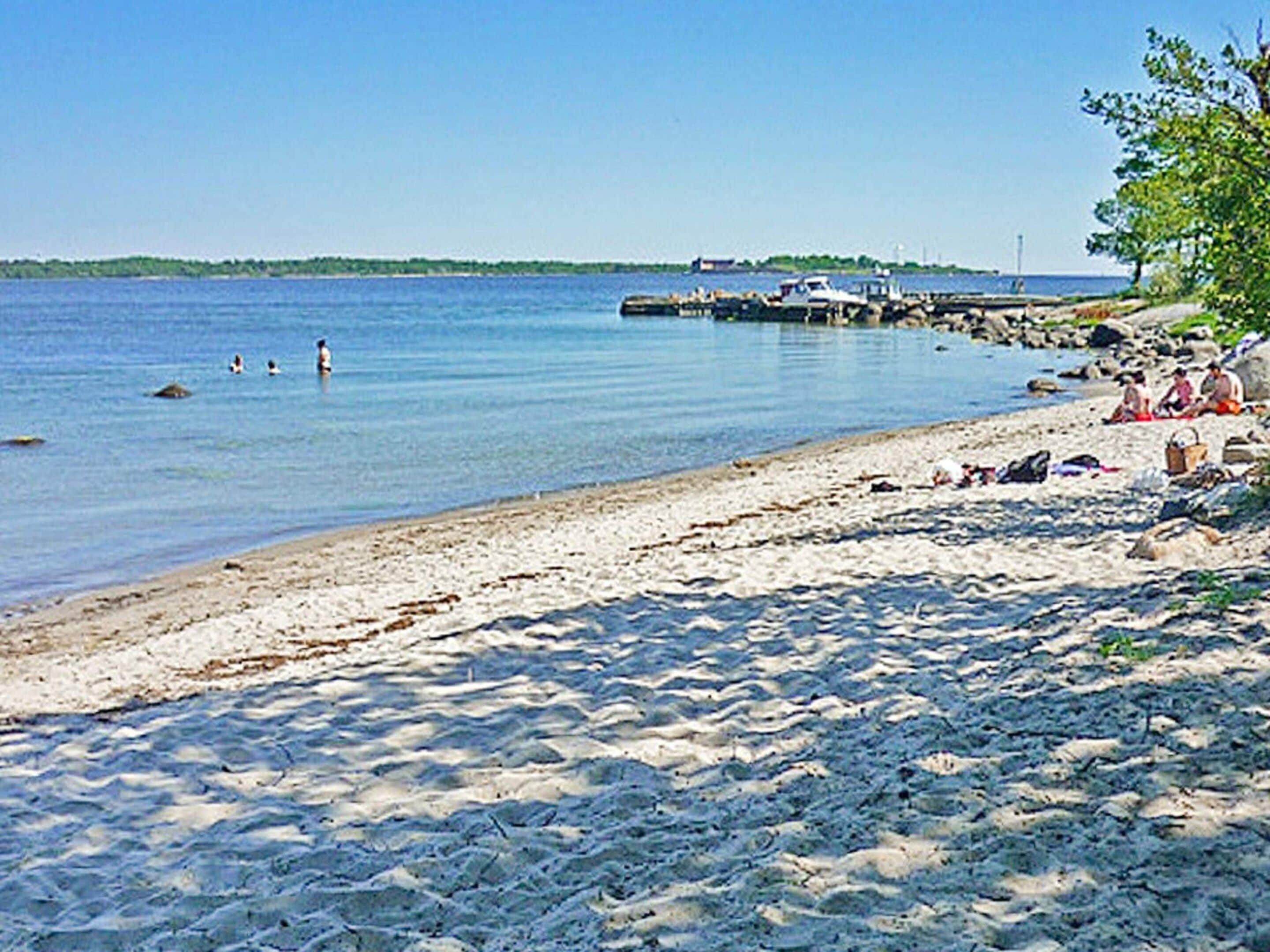 A sandy beach with calm water, a dock, and a few people.