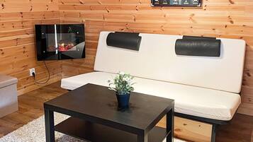 Una habitación con pared de madera, un sofá blanco, una mesa de centro negra y un televisor de pantalla plana montado en la pared.