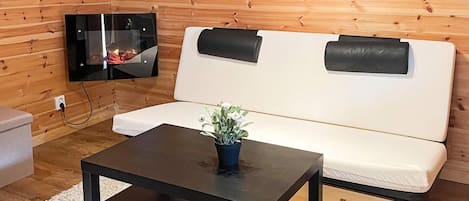 A room with a wooden wall, a white sofa, a black coffee table, and a flat-screen TV mounted on the wall.