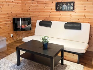 A room with a wooden wall, a white sofa, a black coffee table, and a flat-screen TV mounted on the wall. - 4 Person Holiday Home in Drottningskar (Drottningskär)