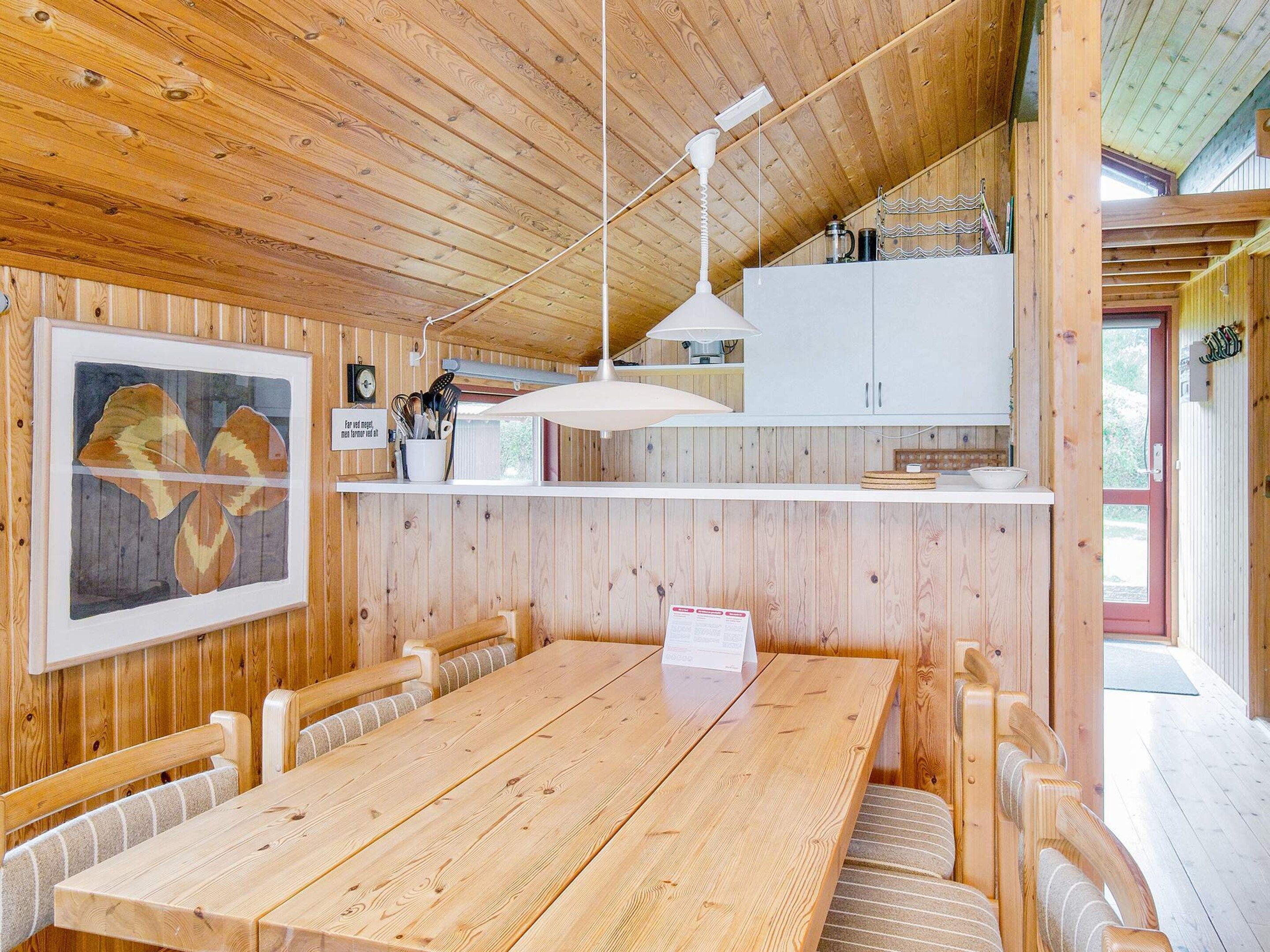 A wooden interior with a dining table, chairs, a kitchen area with cabinets, and a framed picture on the wall.