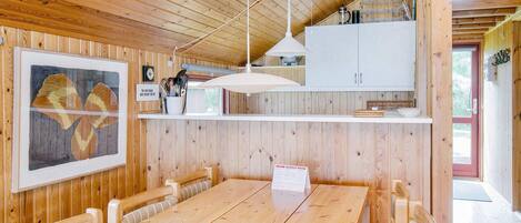 A wooden interior with a dining table, chairs, a kitchen area with cabinets, and a framed picture on the wall.