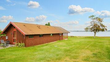 A red wooden building with a sloped roof, a covered porch, and a grassy lawn.