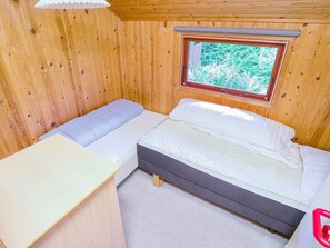 A small wooden cabin room with a bed, a desk, and a window with a view of trees. - 5 Person Holiday Home in Jaegerspris (Jægerspris)