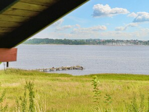 A view of a lake with a dock extending into the water, surrounded by grassy areas and a distant shoreline with buildings. - 5 Person Holiday Home in Jaegerspris (Jægerspris)