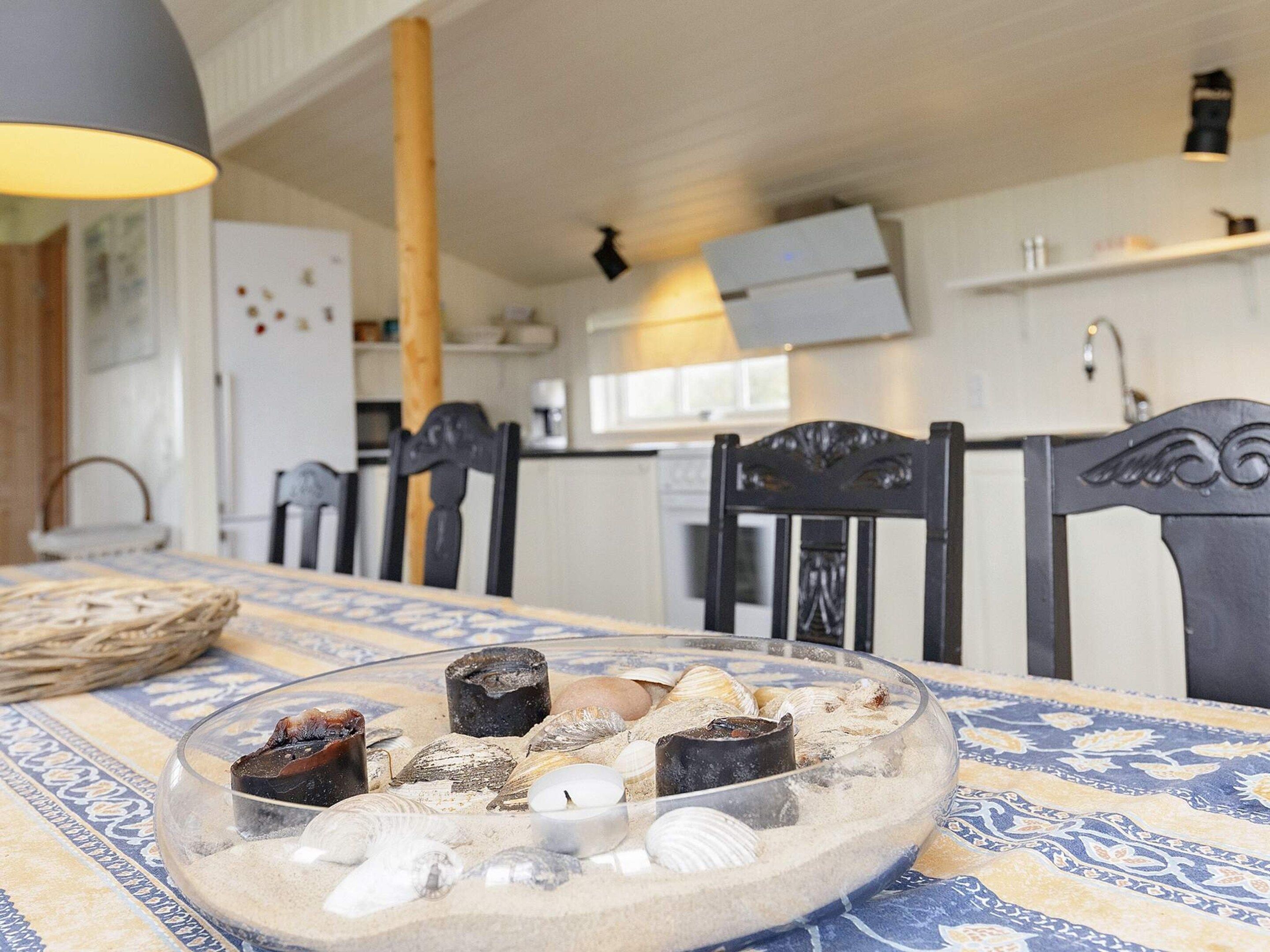 Mesa de jantar com um arranjo de vidro contendo conchas e velas, rodeada por cadeiras.