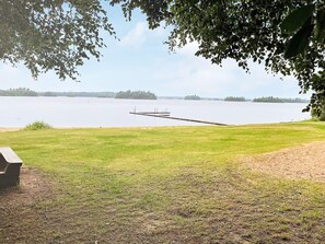 A grassy area with a dock extending into a calm lake, surrounded by trees.