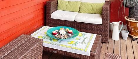A wicker outdoor seating area with a table set for two, a potted plant, and a brick wall in the background.