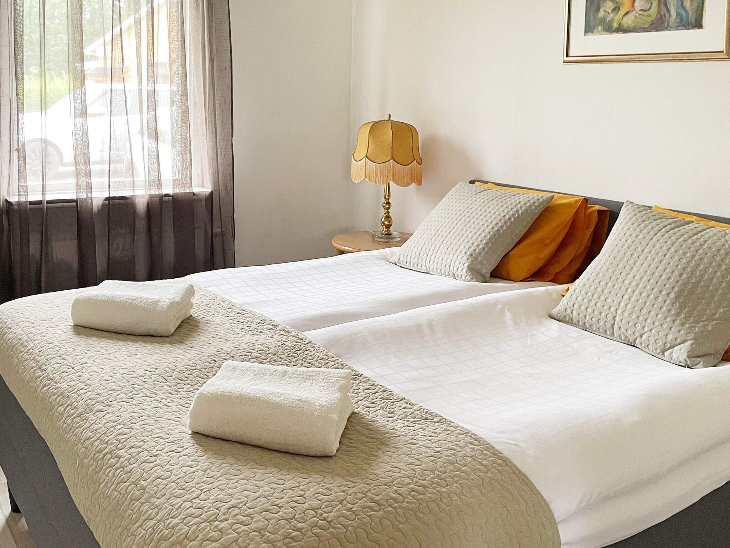 A double bed with two pillows and a blanket, a bedside lamp, and a window with curtains.