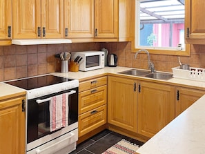 A kitchen with wooden cabinets, a microwave, a stove, and a sink. - 4 Star Holiday Home in Dio (Diö)