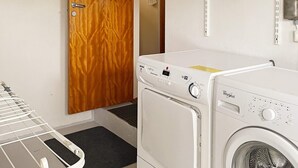 A laundry area with a dryer and a washing machine, a wooden door, and a metal drying rack. - 4 Star Holiday Home in Dio (Diö)