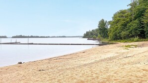 A sandy beach with a calm body of water, a dock, and a forested area in the background. - 4 Star Holiday Home in Dio (Diö)