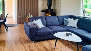 A modern living room with a sectional sofa, a round coffee table, and a wood-burning stove. - 6 Person Holiday Home in Hadsund (Hadsund)