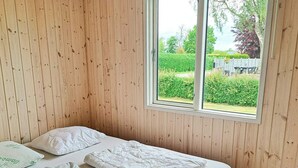 A room with wooden panel walls, a single bed with white bedding, and a window with a view of a garden. - 6 Person Holiday Home in Hadsund (Hadsund)