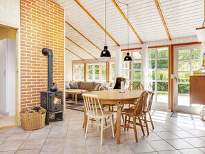 A cozy dining area with a brick wall, a wood-burning stove, and a large window providing a view of the outdoors. - 8 Person Holiday Home in Jerup (Strandby)