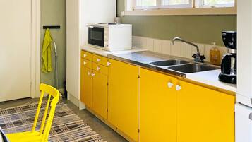 A kitchen with yellow cabinets, a white countertop, a sink, a microwave, a coffee maker, and a window above the sink.