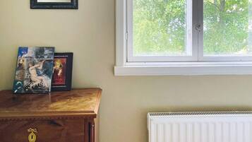 A room with a wooden dresser, two books, a mirror, and a window with a view of trees.