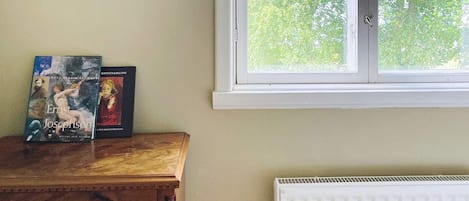 A room with a wooden dresser, two books, a mirror, and a window with a view of trees.