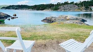 Two white Adirondack chairs facing a lake with rocky shores and a forested hill in the background. - 6 Person Holiday Home in Henan (Henån)