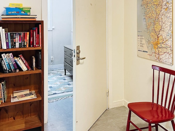 Una habitación con una estantería, un sillón rojo, una puerta que da a otra habitación y un mapa en la pared.
